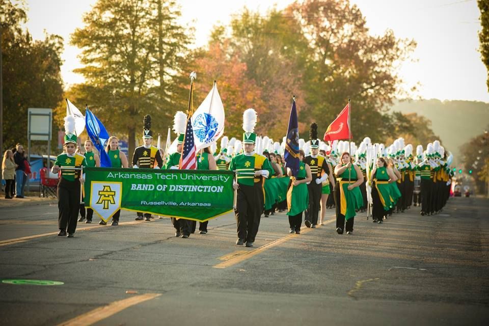 Marching band in green uniforms leads a parade with flags and a green banner reading “REED CONSTRUCTION.”