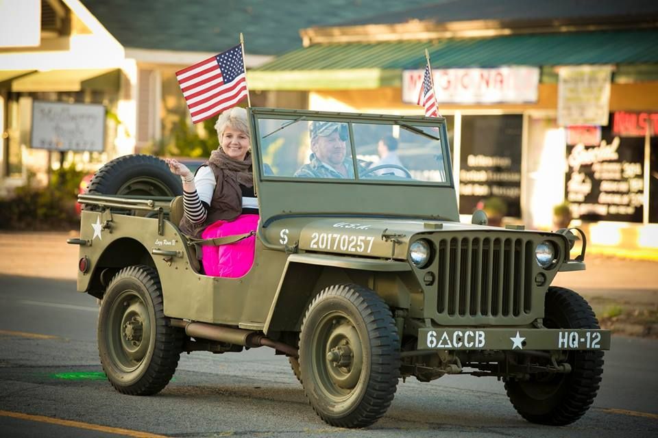 Child riding in a vintage military jeep with small U.S. flags on a street procession