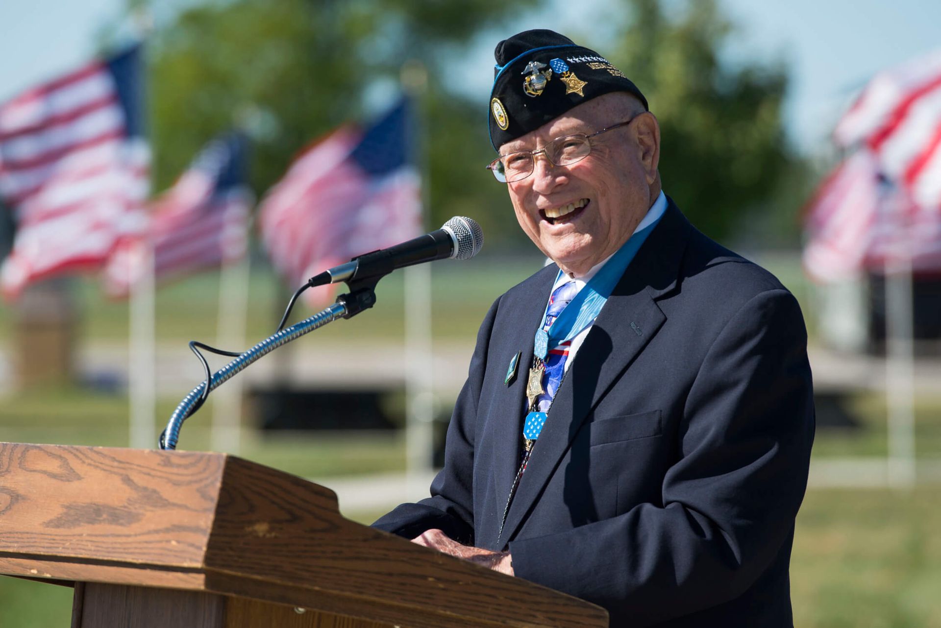 Veteran speaking at a podium outdoors with American flags in the background