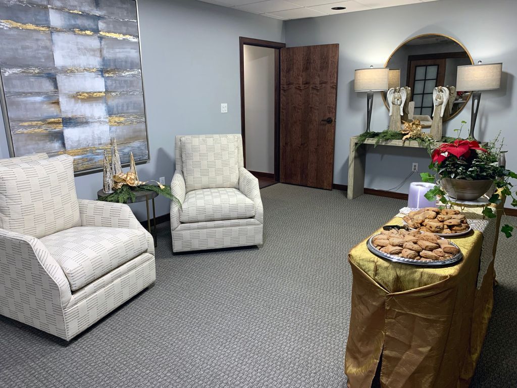 Cozy living room with two white chairs and a buffet table of pastries and flowers.