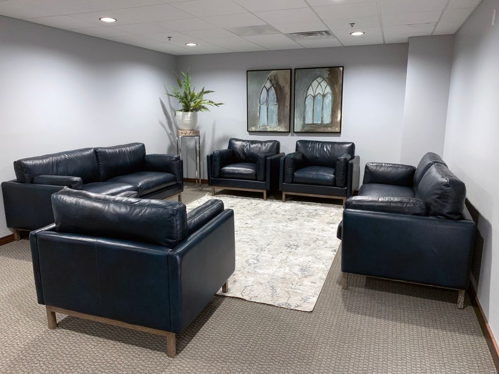 Office waiting room with black leather chairs around a cream rug and a plant by the wall art