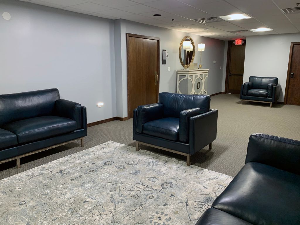 Modern lobby with dark blue leather chairs, patterned rug, wood door, and decorative console table.