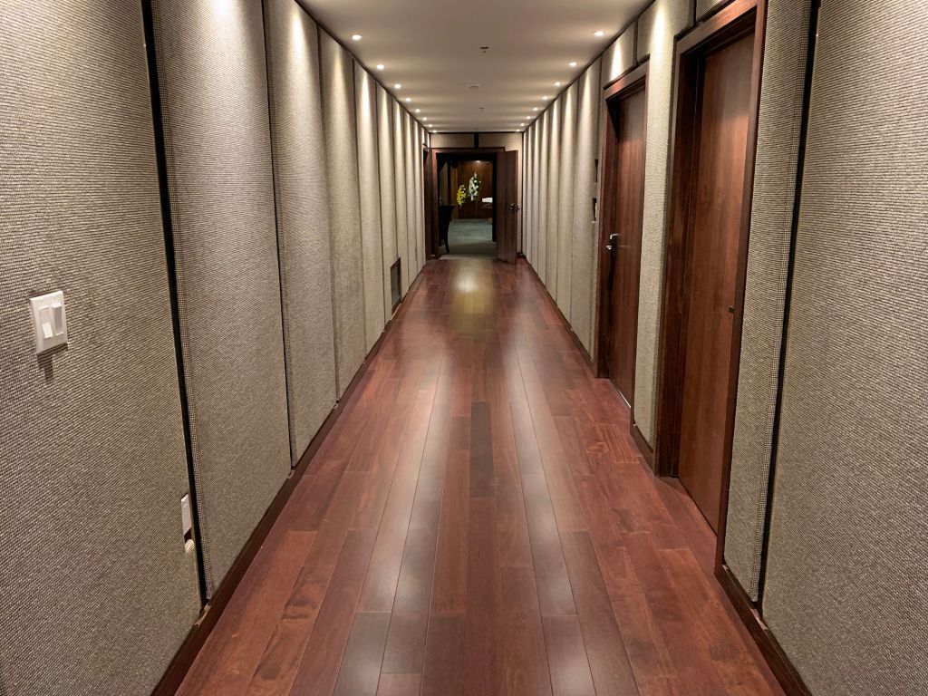 Narrow hotel hallway with wood floors, patterned walls, and closed doors on both sides
