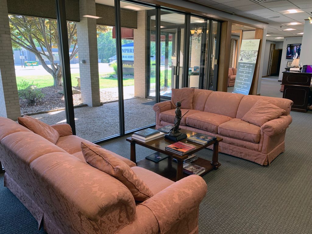 Lobby seating area with two salmon sofas, glass coffee table, and floor-to-ceiling windows facing greenery