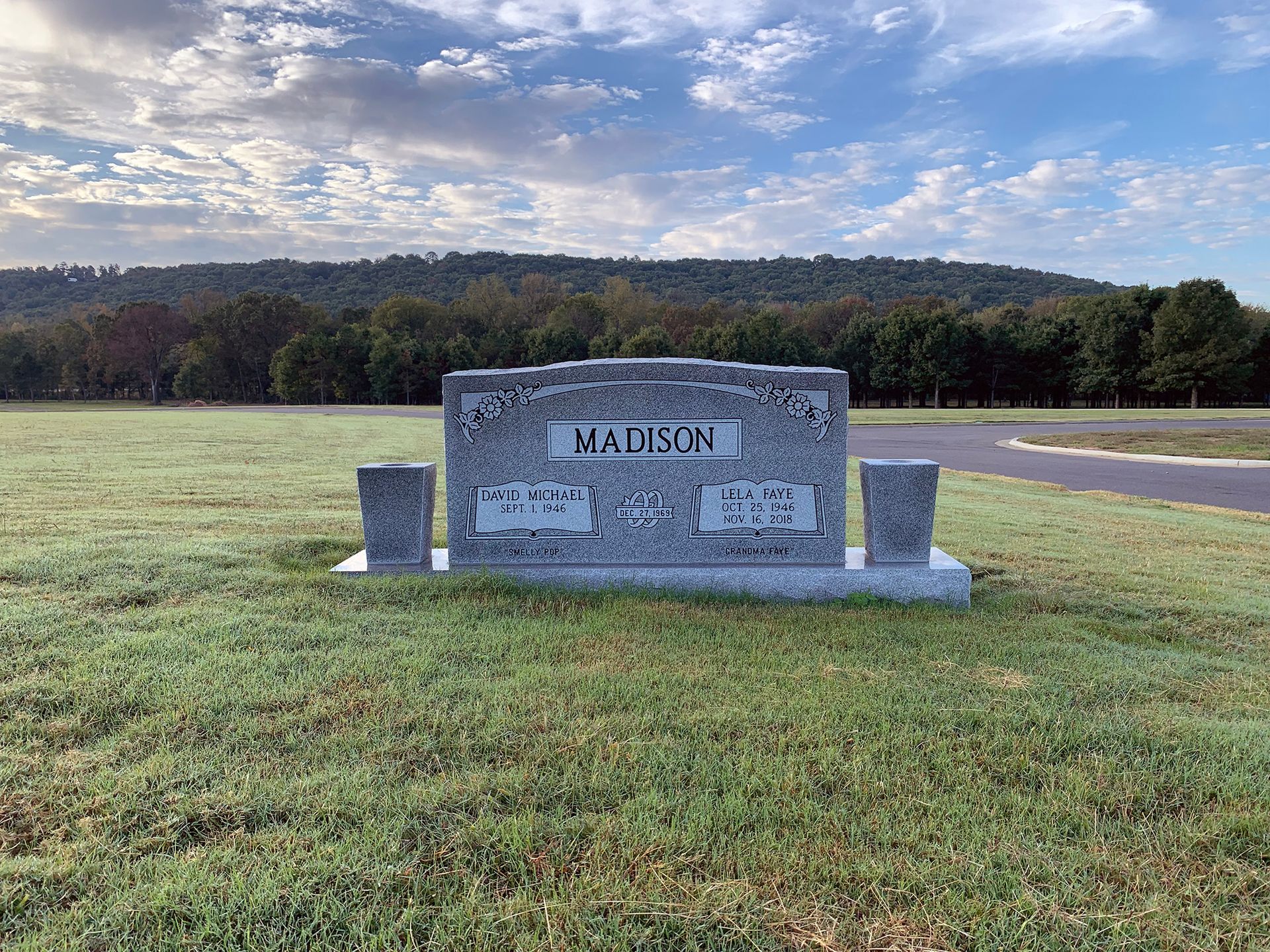 Stone town sign reading “Madison” in a grassy field with trees and a cloudy sky.