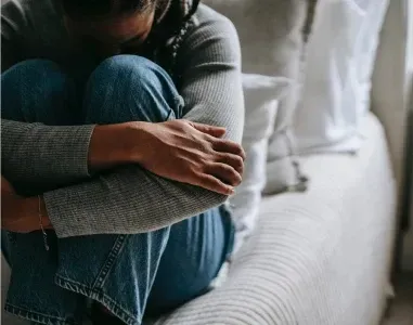 A grieving person sitting with their arms wrapped around their knees in quiet reflection.