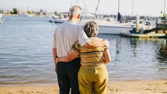 An older couple standing together by the waterfront, symbolizing retirement planning and financial security.