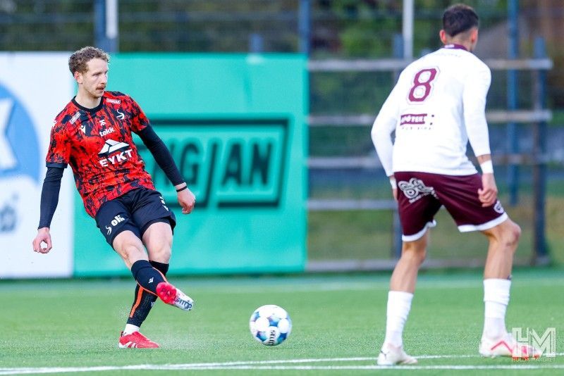 Knattspyrnumaður í rauðum og svörtum treyju dribblar boltann á vellinum í leik