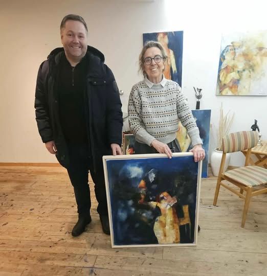 Tveir einstaklingar í listasafni halda á stóru innrammuðu málverki við hliðina á öðrum listaverkum.
