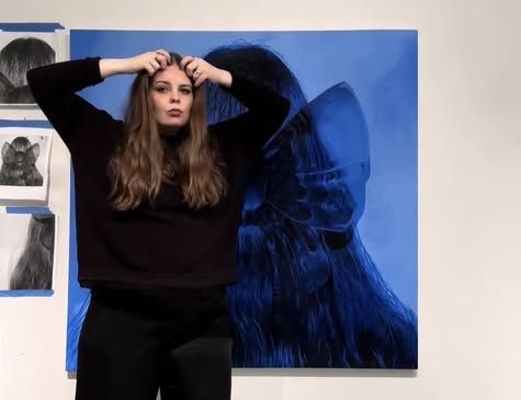 Kona situr fyrir framan blátt portrettmálverk á vegg í galleríi