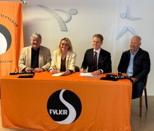 Fjórir einstaklingar sitja fyrir aftan appelsínugult FYLKIR borð á blaðamannafundi eða fundi