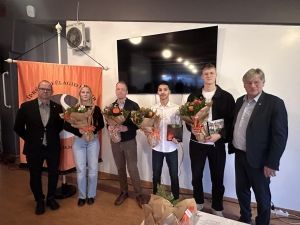 Sex manns á sviði halda á blómvöndum á verðlaunaafhendingu.