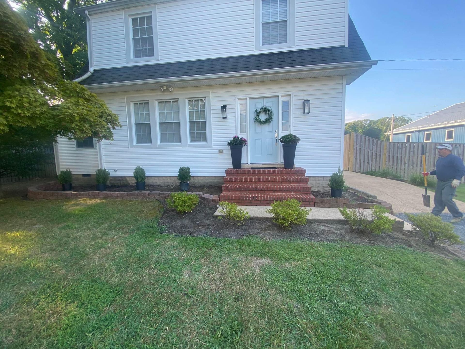 White two-story house with front steps, small garden, and a person walking on the driveway.