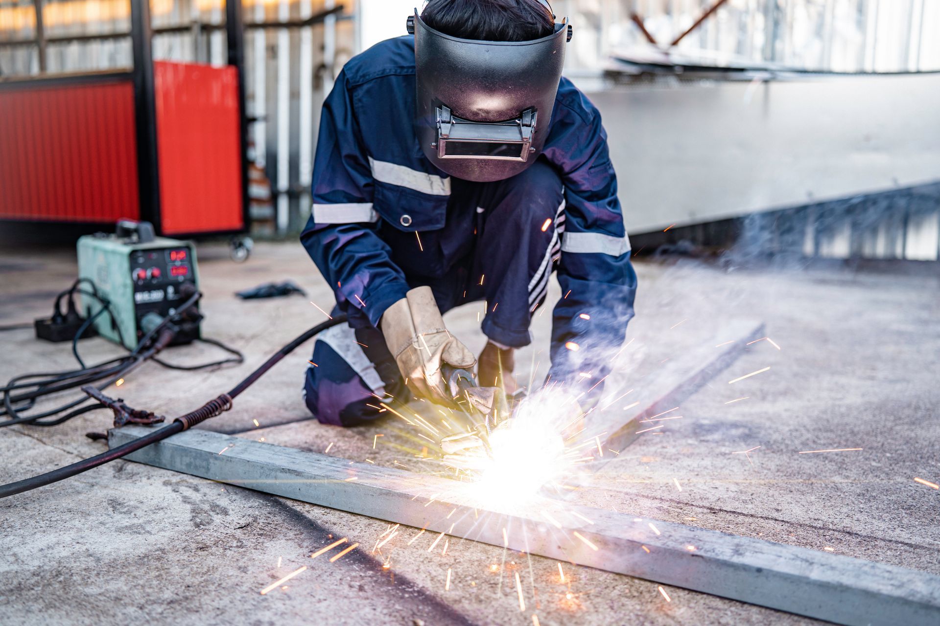Male worker welding metal workpiece outside factory.