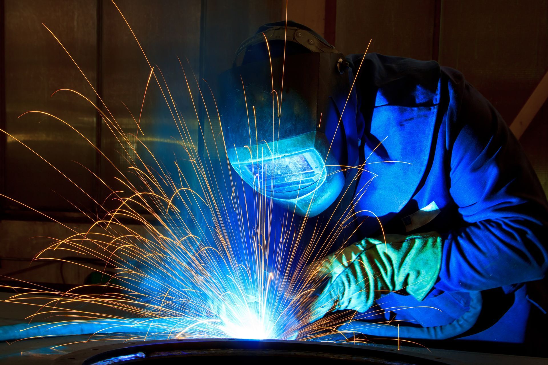 a welder working on metal, producing bright blue light and orange sparks.
