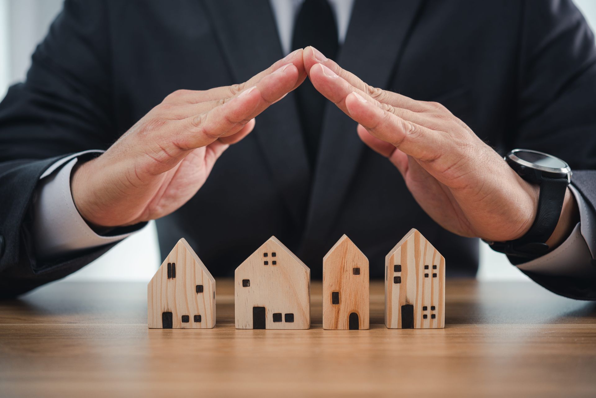Hands protecting small wooden houses on a table, symbolizing home insurance or property protection