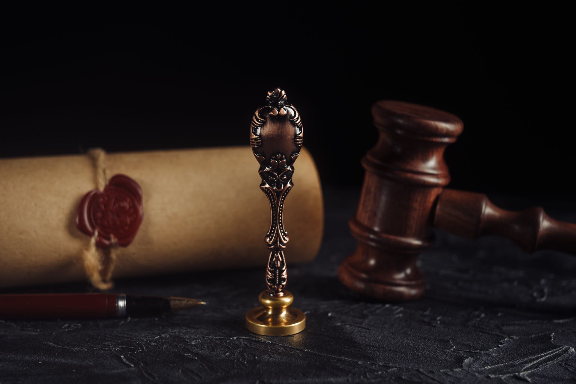 Wooden gavel, rolled legal scroll with wax seal, and ornate stamp on a dark desk