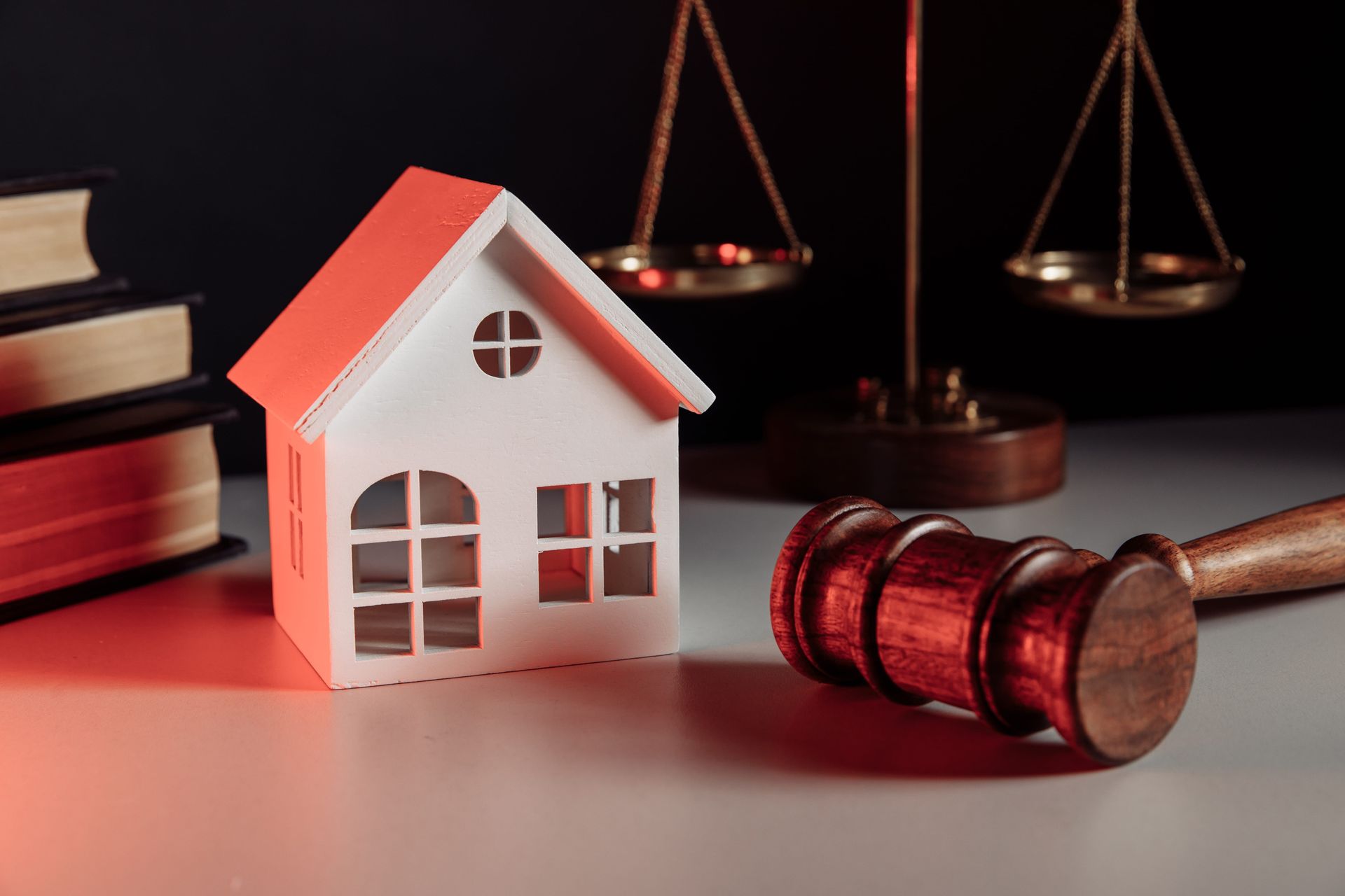 Toy house and judge’s gavel on a desk with scales of justice in the background