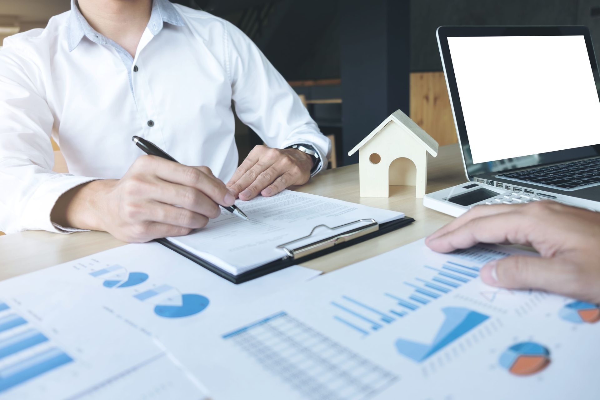 Person reviewing financial charts and a house model during a real estate meeting