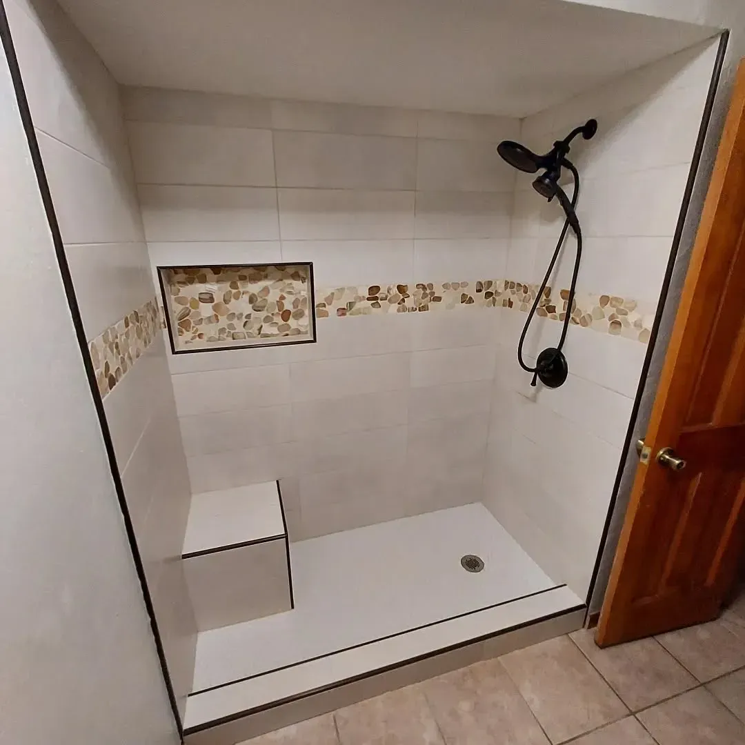 Accessible shower with white tile, black fixtures, and a stone accent niche.
