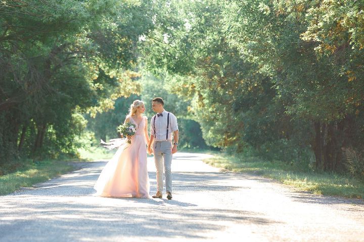 A bride and groom are walking down a road holding hands.