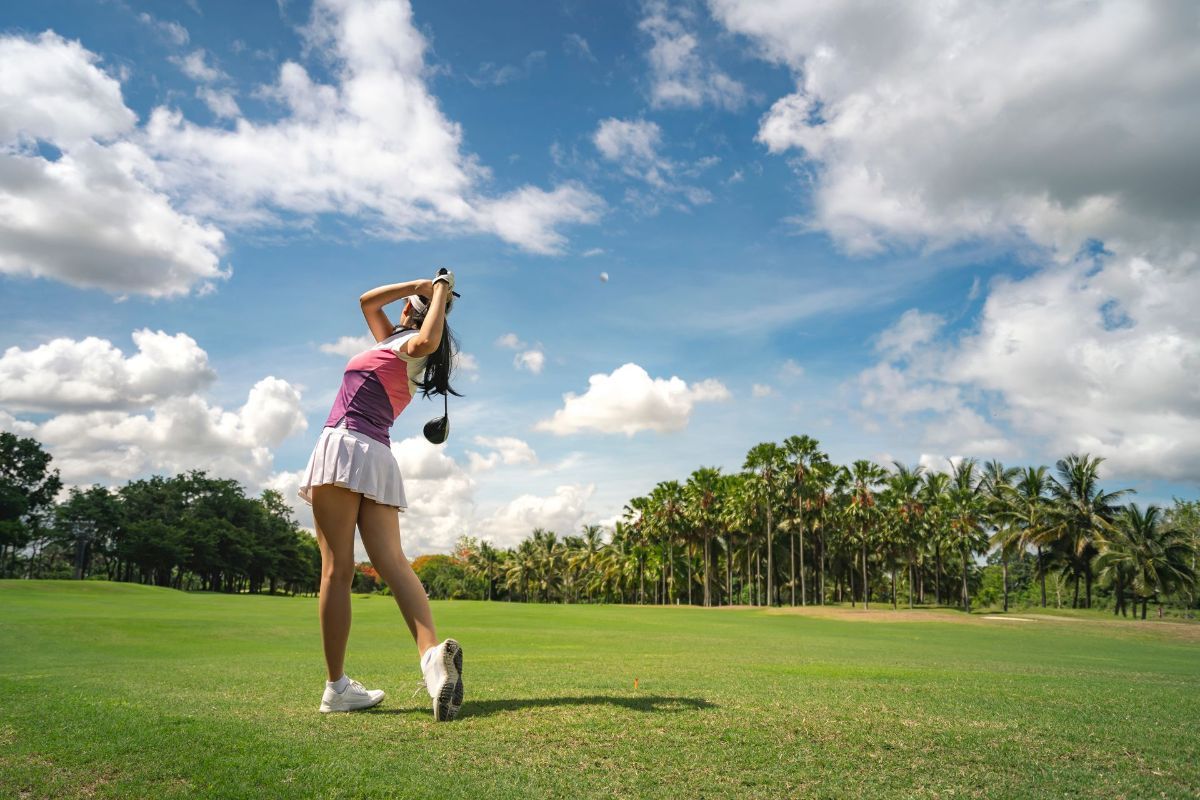 A woman is swinging a golf club on a golf course.
