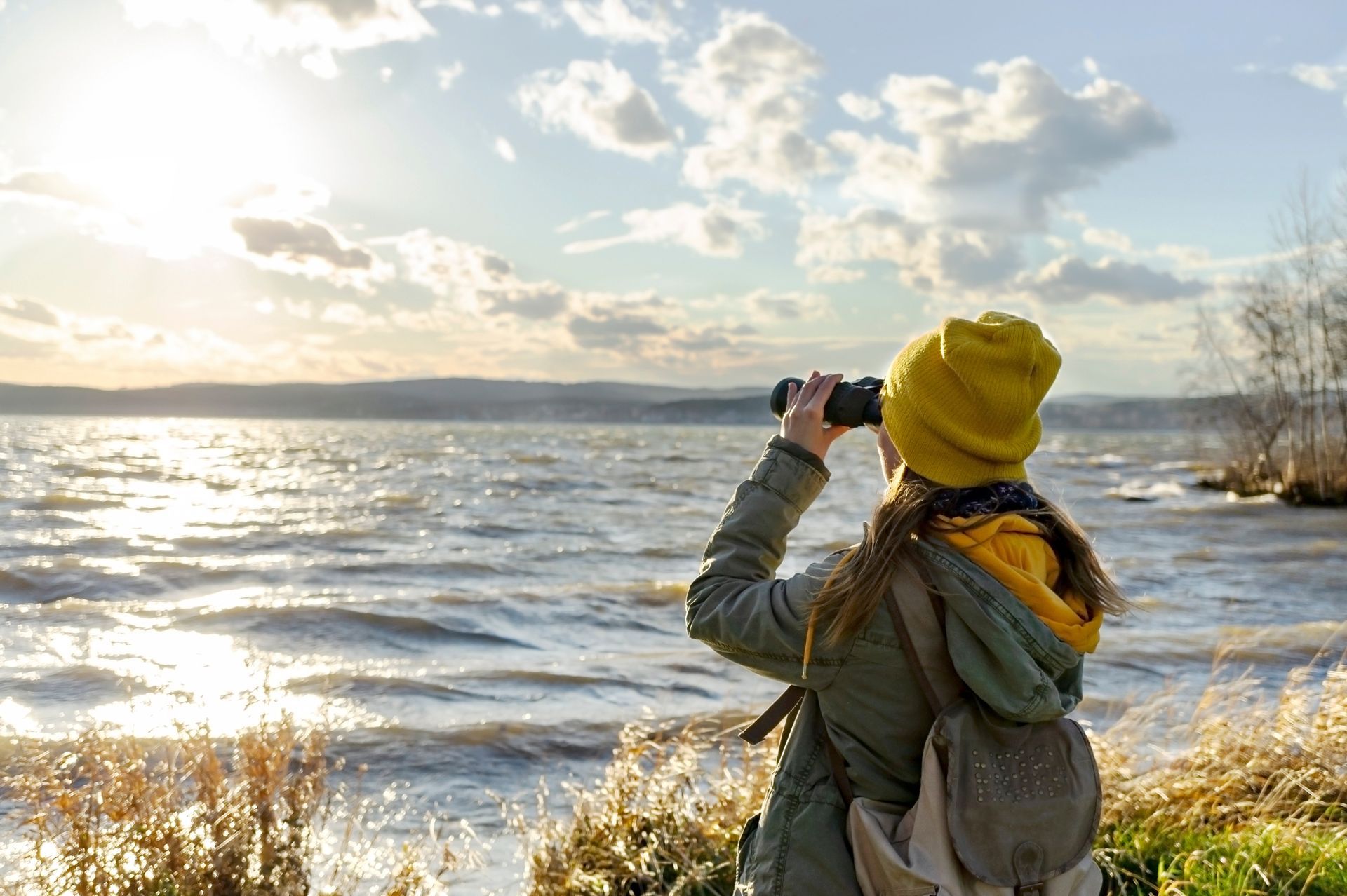 A woman is looking through binoculars at a lake.