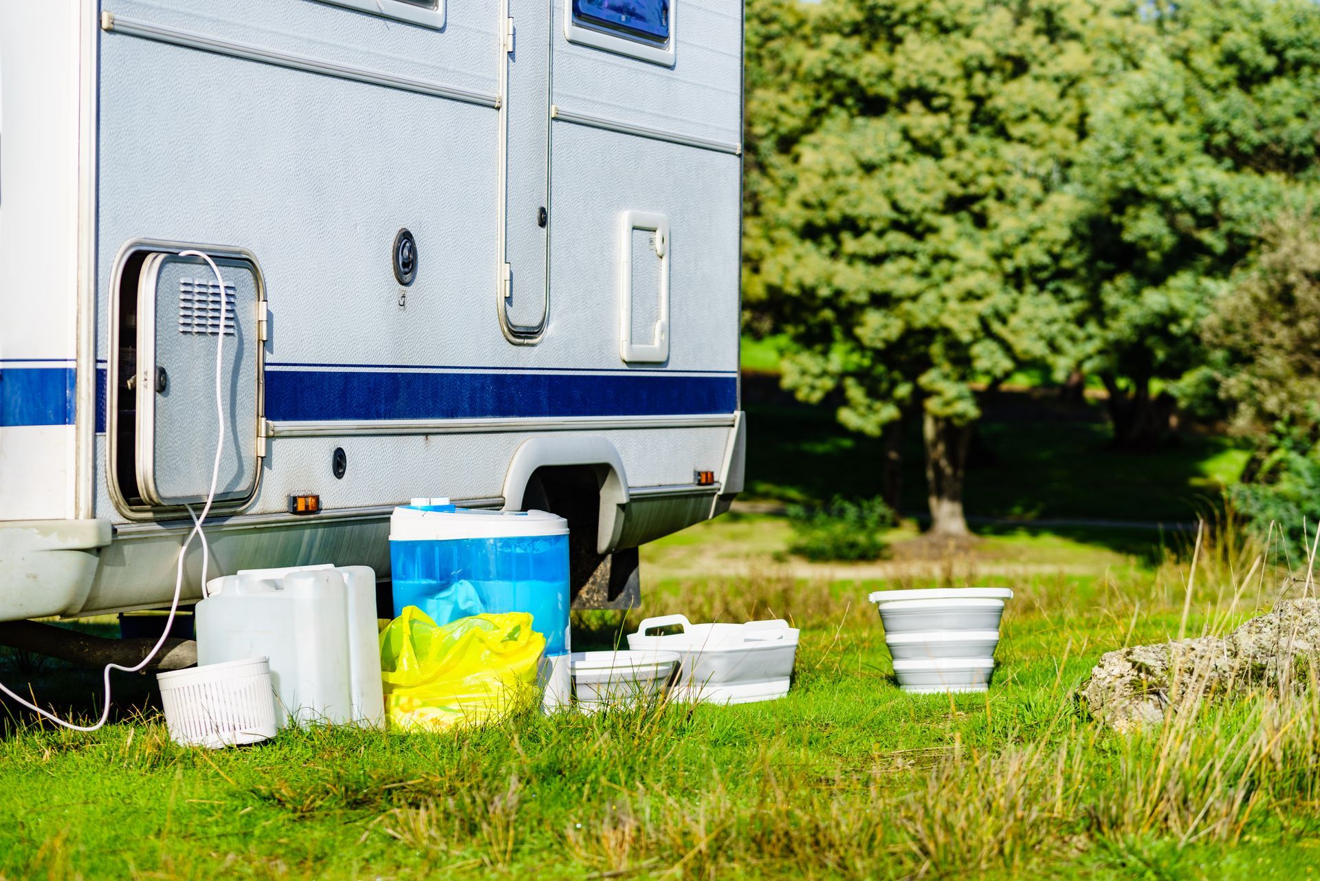 A rv is parked in a grassy field with buckets and coolers.