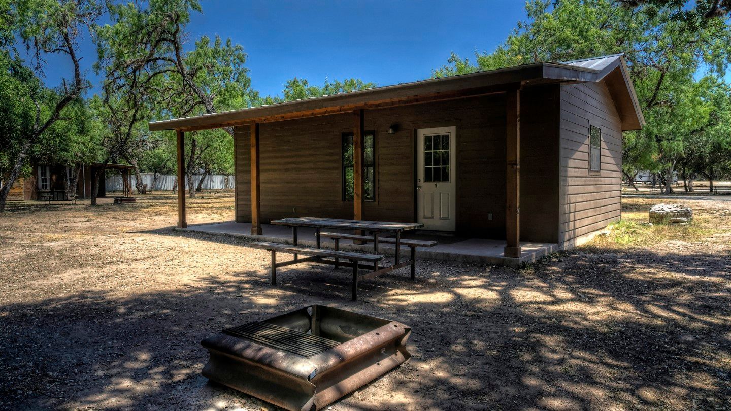 A small cabin with a picnic table and a fire pit in front of it.