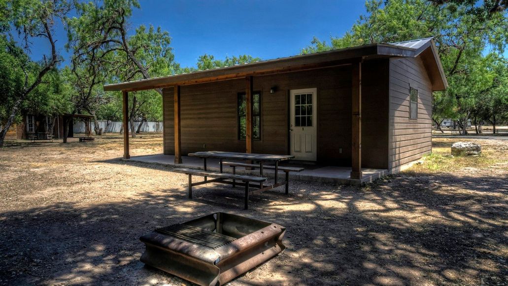A small cabin with a picnic table and a fire pit in front of it.