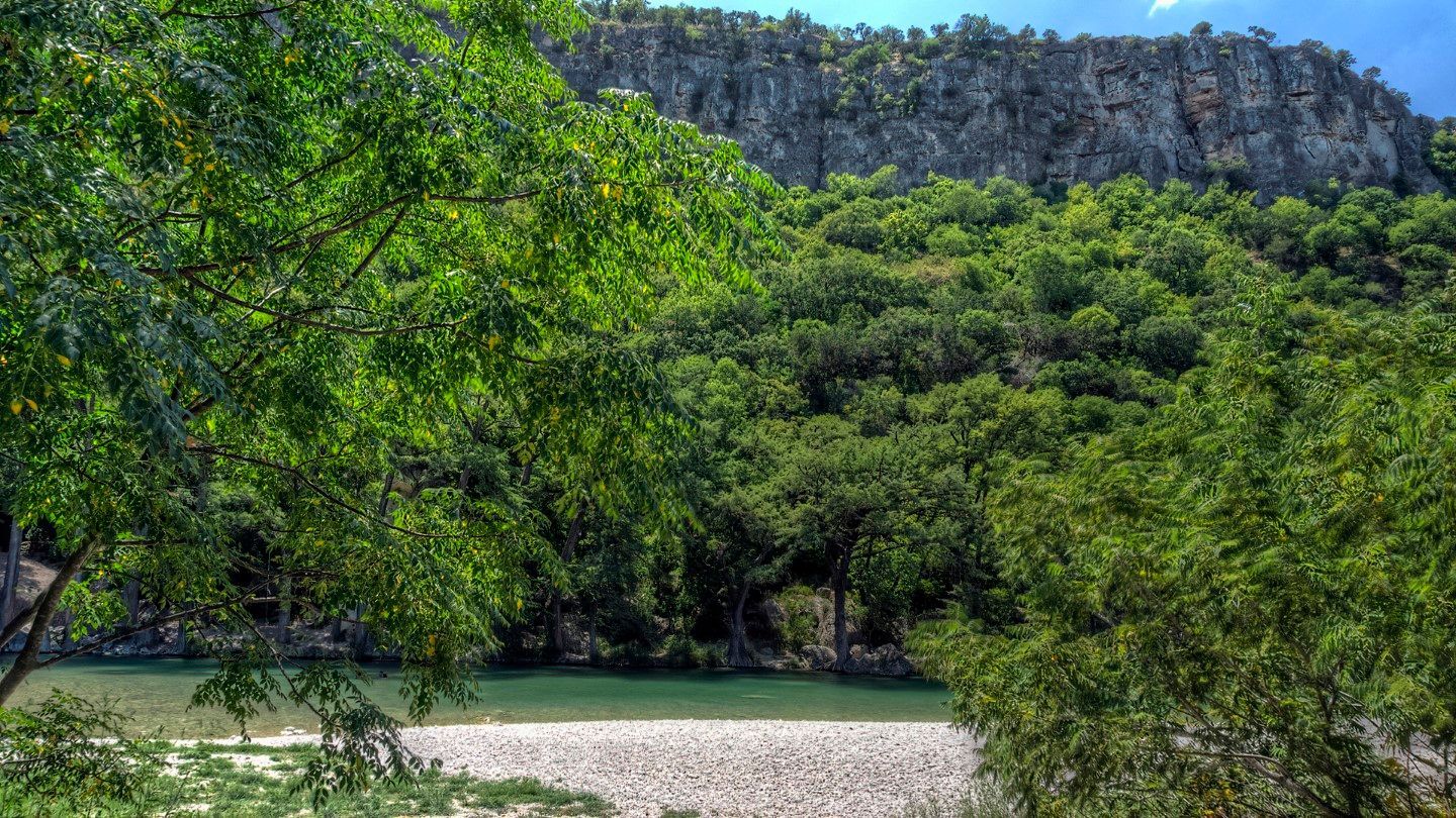 A river surrounded by trees and mountains with a cliff in the background.