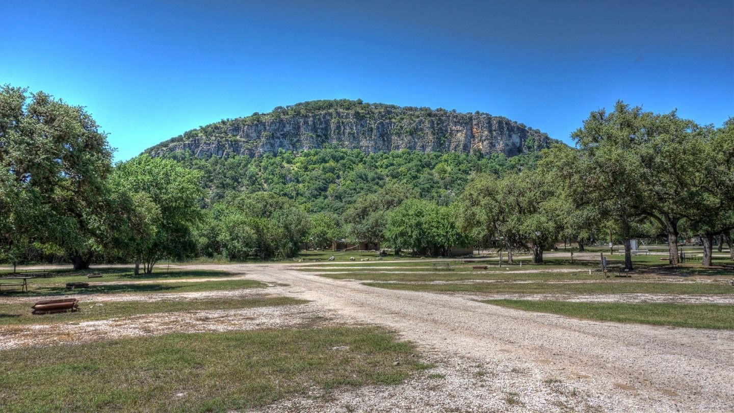 A dirt road going through a park with trees and a mountain in the background.