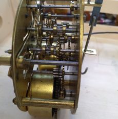 Close-up of a brass clock movement mechanism with exposed gears and plates held together by metal spacers.