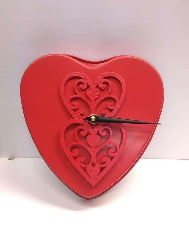 A red, heart-shaped wall clock decorated with intricate, laser-cut heart patterns and a single black clock hand.