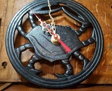 A black, circular cast-iron wall clock shaped like a crab with ornate gold hands, mounted on a wooden surface.