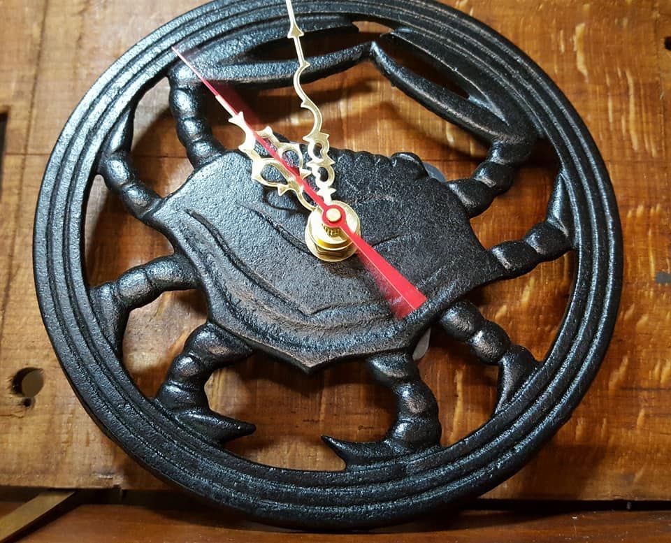 A circular wall clock featuring a dark metal crab sculpture as the face, mounted on a wooden surface.