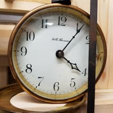 A vintage Seth Thomas clock with a white face, black numerals, and delicate hands, set against a wood background.