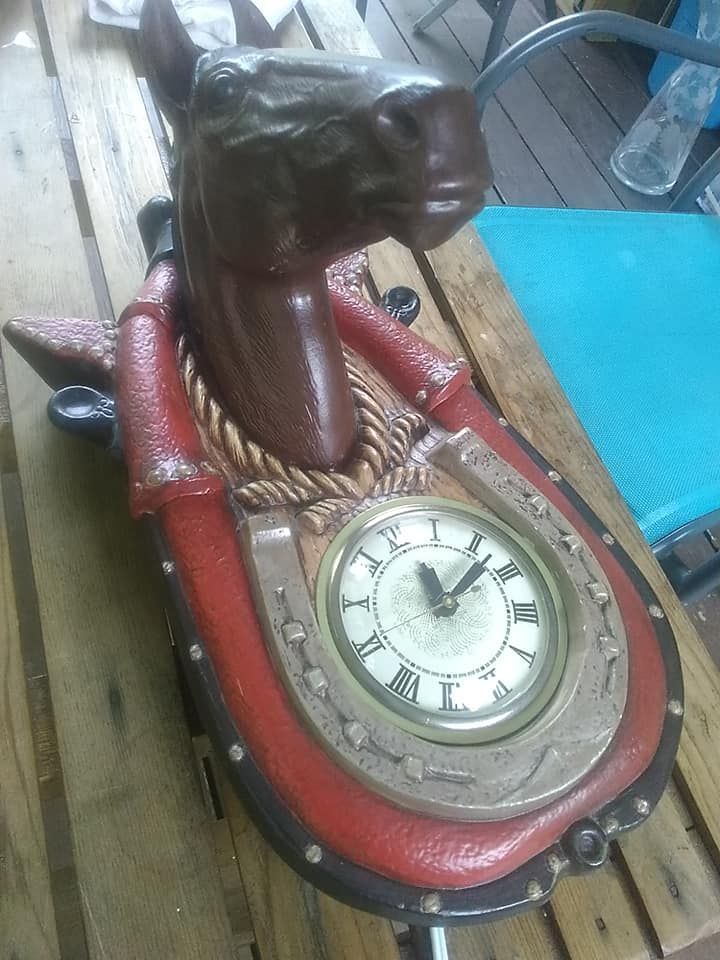 A wall clock shaped like a horse head framed by a red horseshoe on a wooden table.