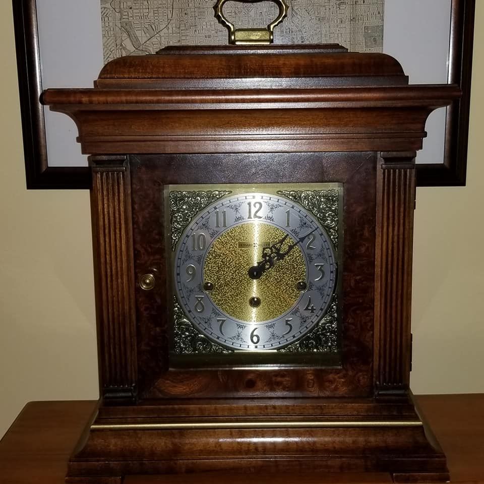 A vintage wooden mantel clock with a decorative brass face and ornate hands sits on a wooden surface.