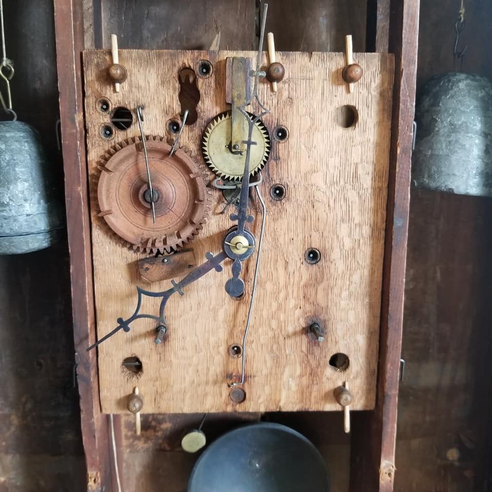 The internal mechanism of a wooden-faced wall clock with visible gears, hands, and hanging weights.