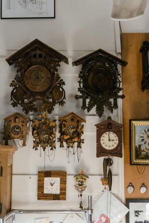 A wall covered in various wooden cuckoo clocks and framed pictures, arranged in a display.