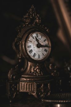 An ornate, antique brass clock sits in dim lighting, its hands indicating a time shortly after ten o'clock.