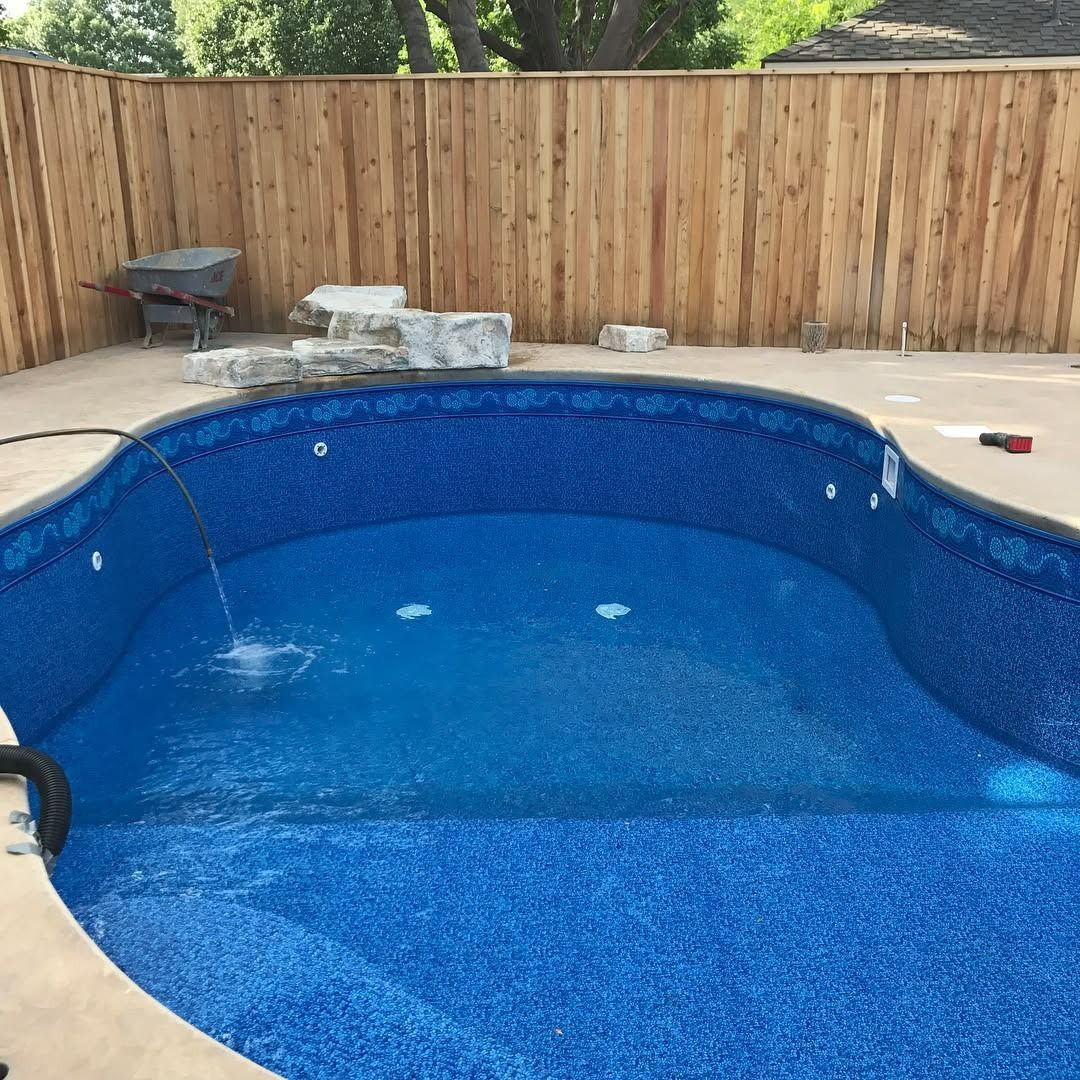 Blue tiled swimming pool, being filled with water, against a wooden fence.
