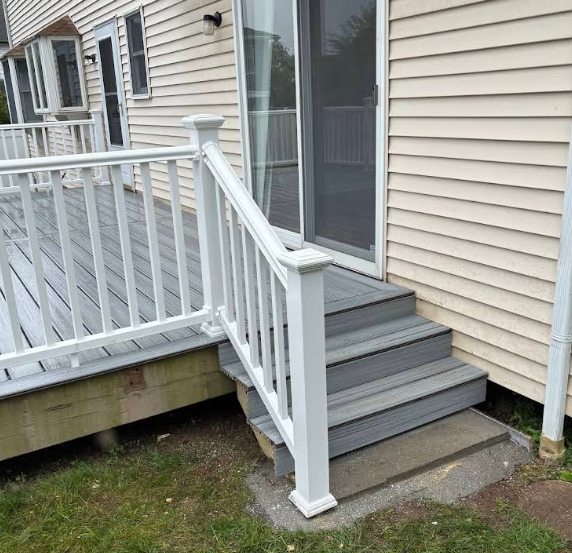 White railing and stairs lead down from a deck to a grassy yard, next to a sliding glass door.