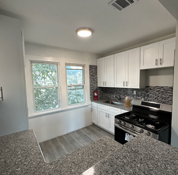 Small kitchen with white cabinets, stainless steel stove, and windows.