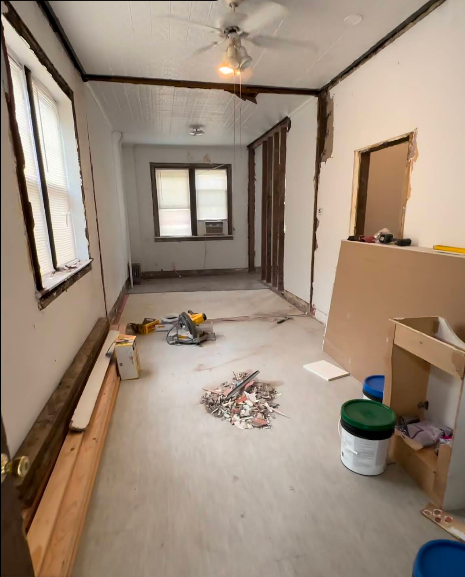 Room under construction; walls exposed, debris on floor, drywall and tools present.