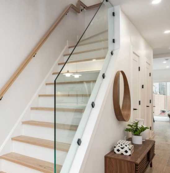 Staircase with wooden steps and railing, glass side panel, and white walls; a wooden console and round mirror are on the right.
