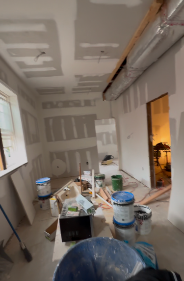 Interior room under construction, drywall, paint buckets, tools, and exposed ductwork.
