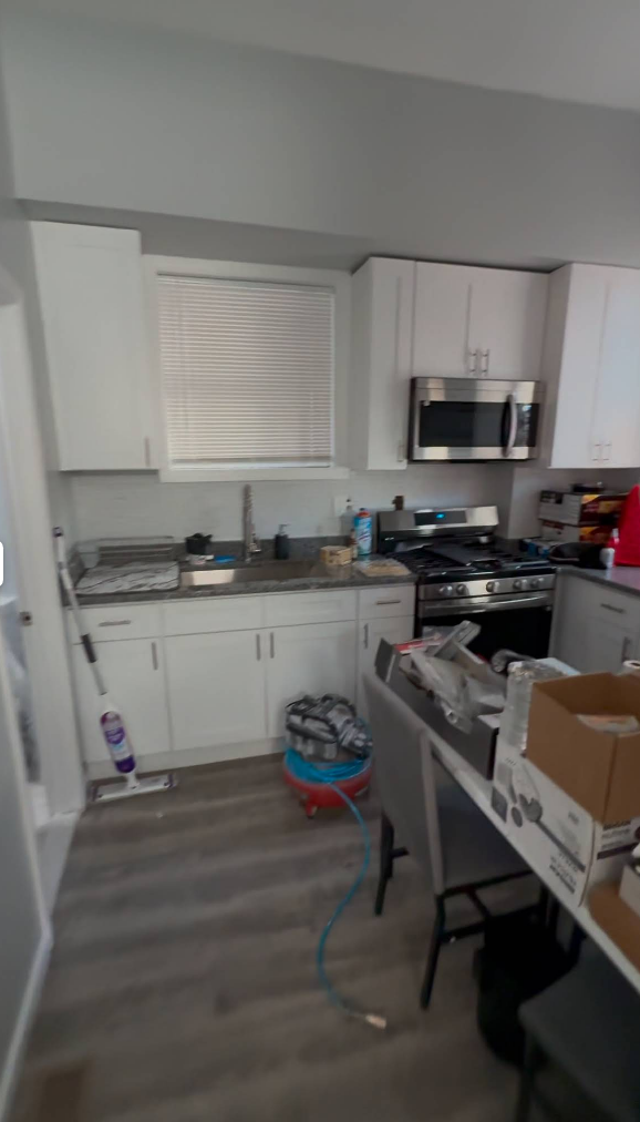 A white kitchen with cabinets, a stainless steel microwave, and a stovetop.