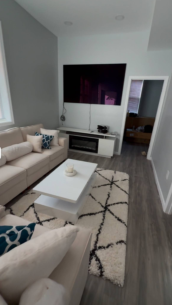 Living room with a large TV, fireplace, white sofa, and a geometric rug.